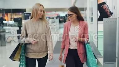 快乐的女人在商店购物中心里拎着纸袋，一边说话，一边打手势。 女孩们穿着